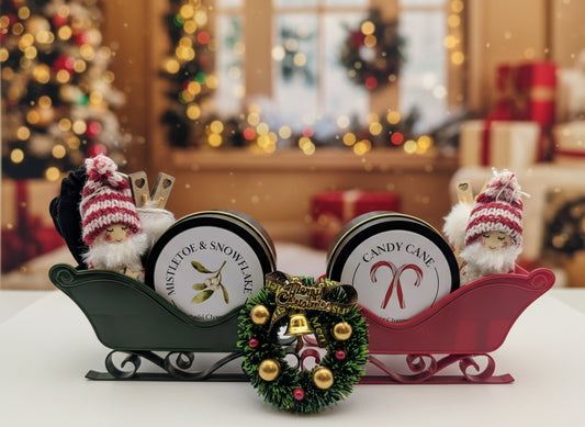 Two holiday-themed tins on a decorative sleigh with small figures and a wreath.