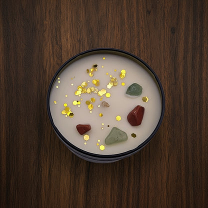 Candle in a black container with gold confetti and colorful stones on a light purple background
