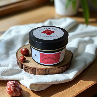 Jar of Root Chakra Candle on a wooden coaster with a white cloth and plant in the background