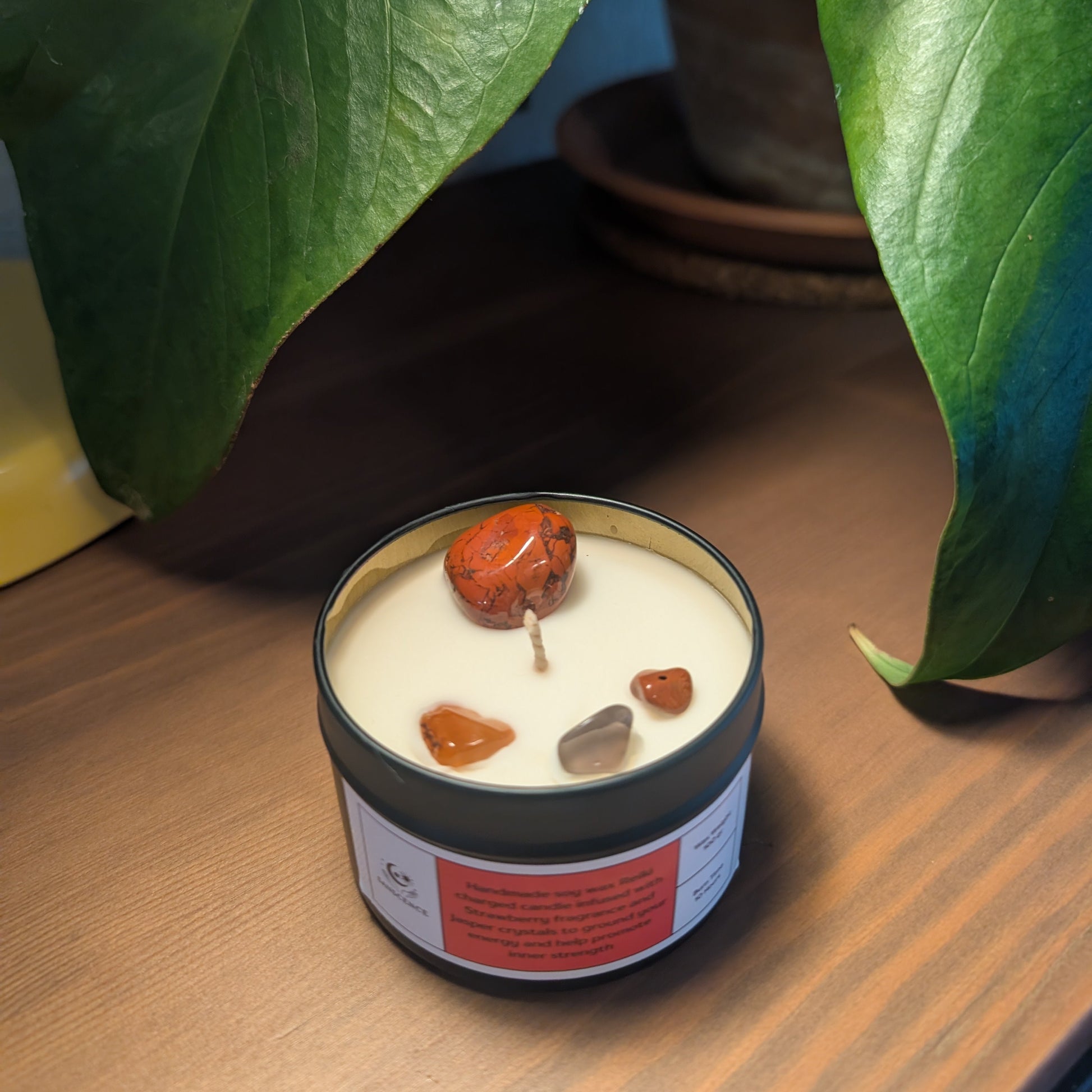 Candle with embedded stones on a wooden surface with plants in the background