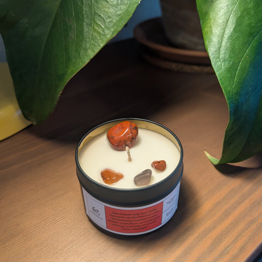 Candle with embedded stones on a wooden surface with plants in the background